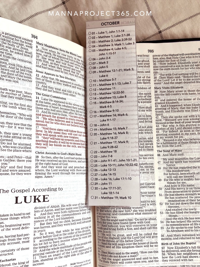 May include: Open Bible with text from the Gospel According to Luke. A clear, rectangular bookmark with the word "October" and a list of Bible readings is placed on the page.