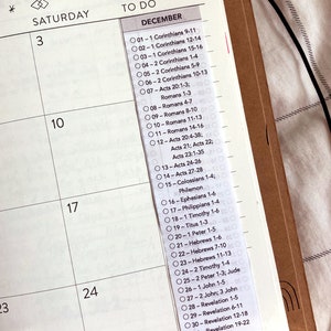 May include: A planner page with a December calendar and a list of Bible verses. The top of the page has decorative tree and star illustrations. The text "TO DO" is above the list of verses. The planner is open to the week of December 3rd.
