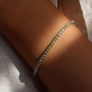 May include: A delicate tennis bracelet with a row of small, sparkling yellow diamonds set in a white metal band.