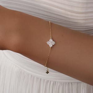 May include: A delicate gold bracelet featuring a four-leaf clover design with sparkling white gemstones. The bracelet is attached to a fine gold chain and is worn on a person's arm.