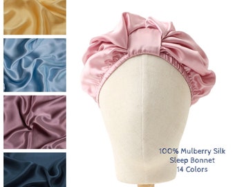 May include: A pink satin sleep bonnet made of 100% mulberry silk. The bonnet is on a white mannequin head. The text "100% Mulberry Silk Sleep Bonnet 14 Colors" is below the bonnet.