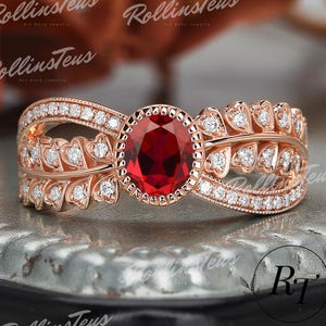 Op de afbeelding: Een ring van roségoud met een grote rode edelsteen omringd door kleinere heldere edelstenen. De ring heeft een delicaat bladontwerp met hartvormige accenten.