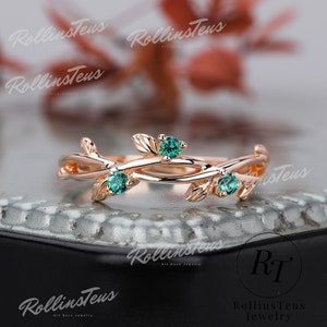 May include: A delicate rose gold ring with a vine design featuring three emerald green gemstones. The ring is a beautiful and unique piece of jewellery.