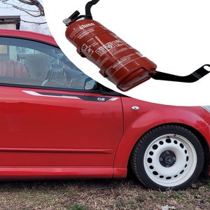 Op de afbeelding: Een rode Citroen C2 VTR met witte velgen en zwarte race strepen. De auto heeft een brandblusser aan de zijkant gemonteerd.