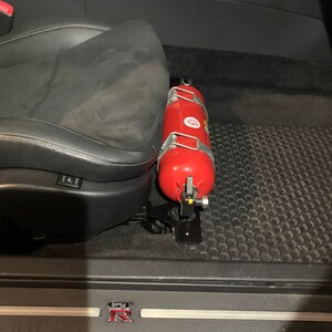 Nissan GTR R35 fire extinguisher holder bracket mounted on OEM seat rails. Ensure safety with this easy-to-access and sturdy bracket for emergencies. Perfect fit for your GTR R35