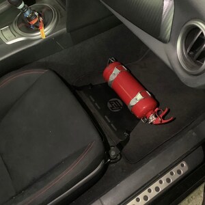 Toyota GT86 fire extinguisher holder bracket mounted on OEM seat rails. Ensure safety with easy access to the fire extinguisher while driving. A reliable addition to your GT86 for emergency situations