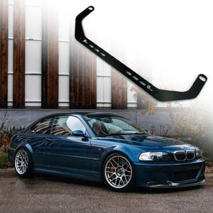 May include: A blue BMW M3 with a black aftermarket strut bar. The car is parked in front of a building with large windows.