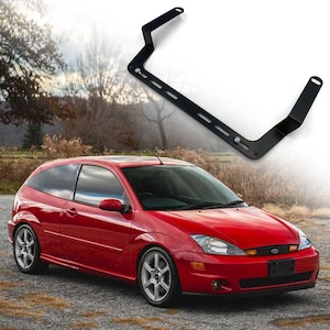 Może przedstawiać: Czerwony samochód typu hatchback ze srebrnymi felgami stoi na żwirowej nawierzchni. Czarny metalowy wspornik z wieloma otworami i punktami montażowymi jest umieszczony nad samochodem.