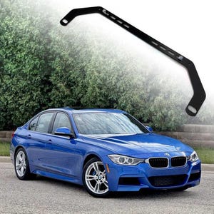 Może przedstawiać: Niebieski sedan BMW serii 3 z czarną belką rozpórkową. Samochód jest zaparkowany na utwardzonej powierzchni z zielonymi drzewami w tle.