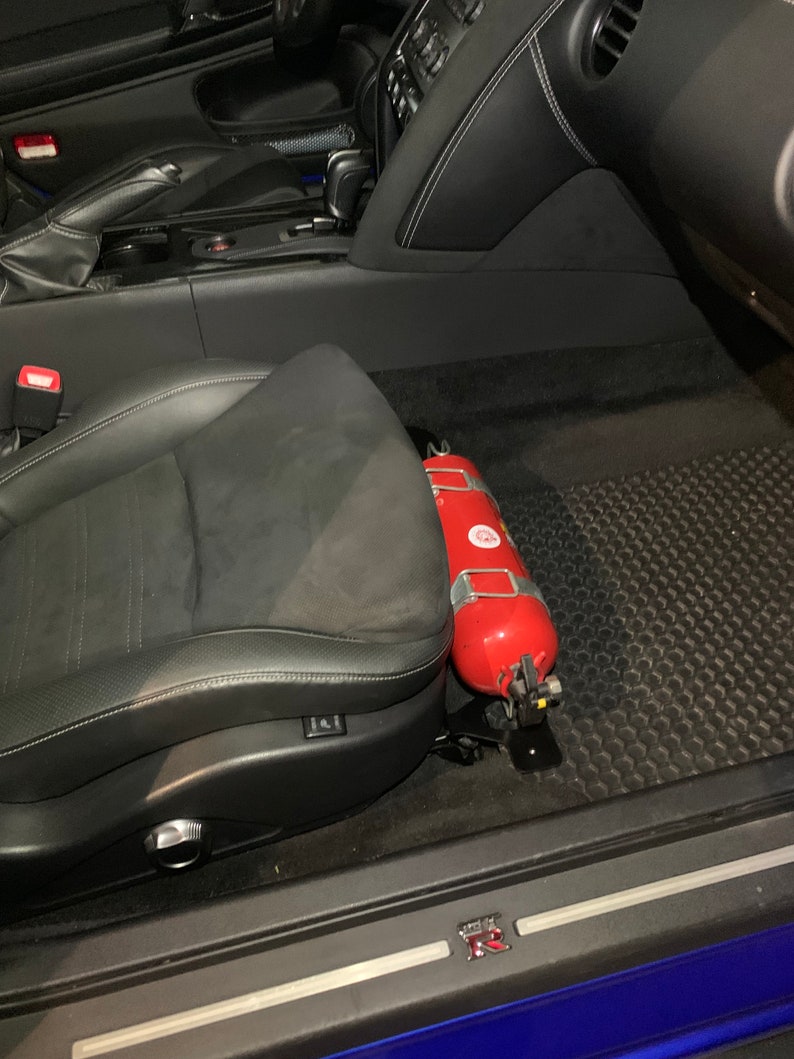 Nissan GTR R35 fire extinguisher holder bracket mounted on OEM seat rails. Ensure safety with this easy-to-access and sturdy bracket for emergencies. Perfect fit for your GTR R35