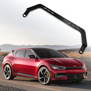 Puede incluir: Un Kia EV6 rojo con llantas negras y un portaequipajes de techo negro. El coche está aparcado en un camino de tierra con un paisaje desértico en el fondo.