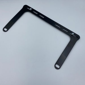 May include: Black metal bracket with two holes on each side and multiple slots along the top. The bracket is designed to be mounted to a wall or other surface.