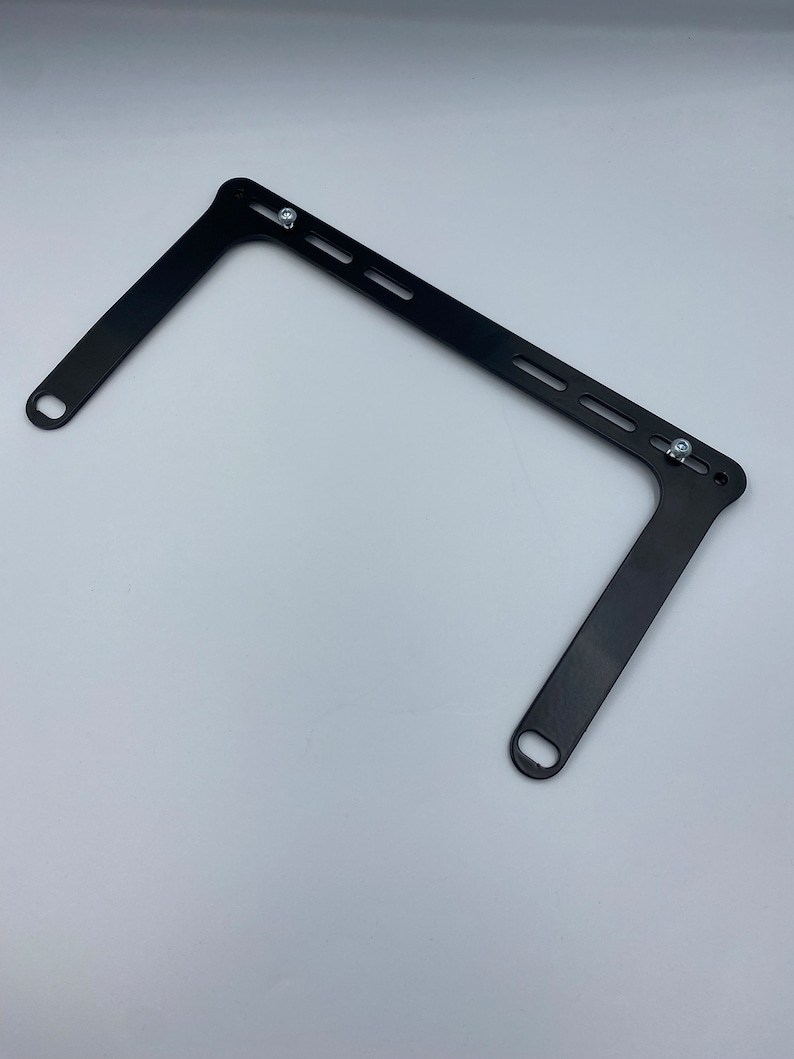 May include: Black metal bracket with two holes on each side and multiple slots along the top. The bracket is designed to be mounted to a wall or other surface.