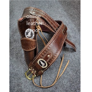 Könnte beinhalten: Brauner Leder-Pistolengürtel mit Holster und einem dekorativen Schnallenverschluss. Der Gürtel hat ein genähtes Design und zwei Metallakzente. Das Holster hat ein Logo mit der Aufschrift "Online Leather Depot".