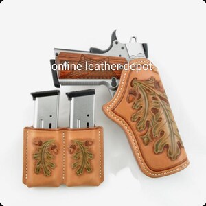 Puede incluir: Una funda de cuero marrón con un diseño de hoja de roble y dos fundas para cargadores a juego. La funda está diseñada para adaptarse a una pistola plateada con empuñadura de madera. El texto "online leather depot" es visible en la imagen.
