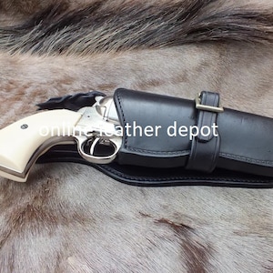 May include: A black leather holster with a silver revolver inside. The holster has a buckle and is designed for a right-handed shooter. The text "online leather depot" is visible on the holster.