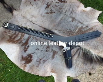 May include: A black leather gun belt with a silver buckle and a silver revolver in a holster. The belt has a cartridge loop with bullets. The text "online leather depot" is visible in the image.