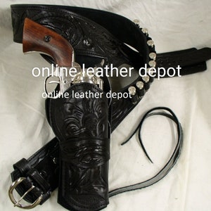 Puede incluir: Juego de cinturón y funda de cuero negro para pistola con un revólver plateado. La funda y el cinturón presentan diseños florales en relieve. El cinturón incluye una hebilla plateada y trabillas para balas.