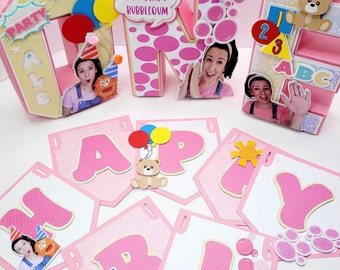 Könnte beinhalten: Rosa und gelbe 'EIN' Geburtstagsdekorationen mit einem 'GLÜCKLICH' Banner. Die Dekorationen zeigen einen Teddybär, Ballons, Blasen und ein Mädchen. Das Banner hat rosa Buchstaben mit weißen Punkten und einem gelben Rand.