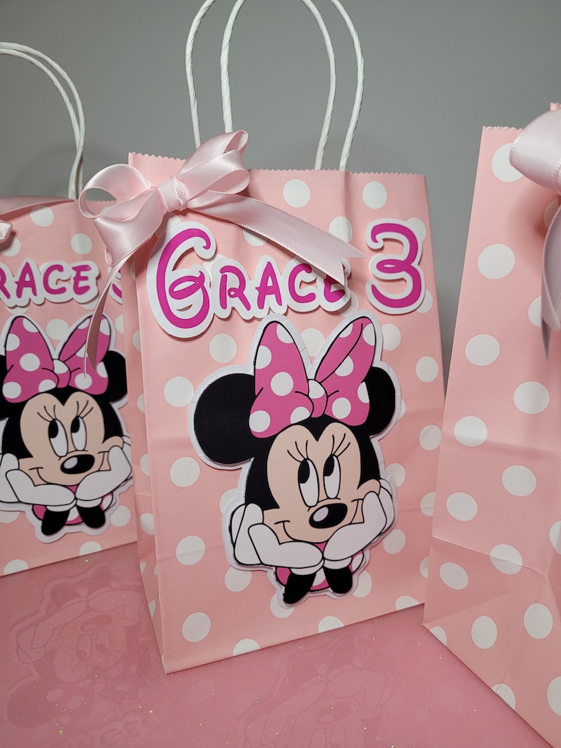May include: Pink and white polka dot gift bags with white handles and pink ribbons. The bags feature a Minnie Mouse character with a pink bow and the name "Grace" and the number "3" in pink.