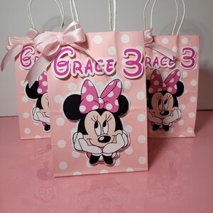 May include: Three pink and white polka dot gift bags with Minnie Mouse character designs. The bags have white satin ribbon bows and the name "Grace 3" is printed on the front of the middle bag.
