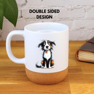 May include: White ceramic mug featuring a cartoon dog illustration. The dog is depicted in black, brown, and white with a yellow collar. The base of the mug is cork. The text "DOUBLE SIDED DESIGN" is printed on the mug.