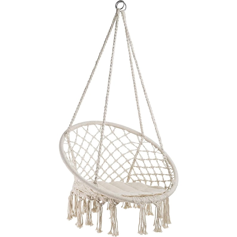 Puede incluir: Una silla colgante blanca con un asiento redondo tejido y detalles de flecos. La silla est&aacute; suspendida de un gancho de metal.