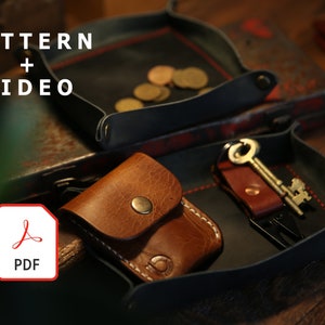 Könnte beinhalten: Ein schwarzes Ledertablett mit roten Nähten, das eine kleine braune Ledertasche, einen Schlüssel mit einem Lederanhänger und ein kleines Werkzeug enthält. Das Tablett liegt auf einer Holzoberfläche. Der Text "PATTERN + VIDEO" ist in der oberen linken Ecke des Bildes sichtbar. Ein rotes PDF-Symbol ist in der unteren linken Ecke des Bildes sichtbar.