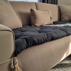 May include: A brown sofa with a black quilted throw blanket and two brown cushions. The sofa has a tassel on the armrest.