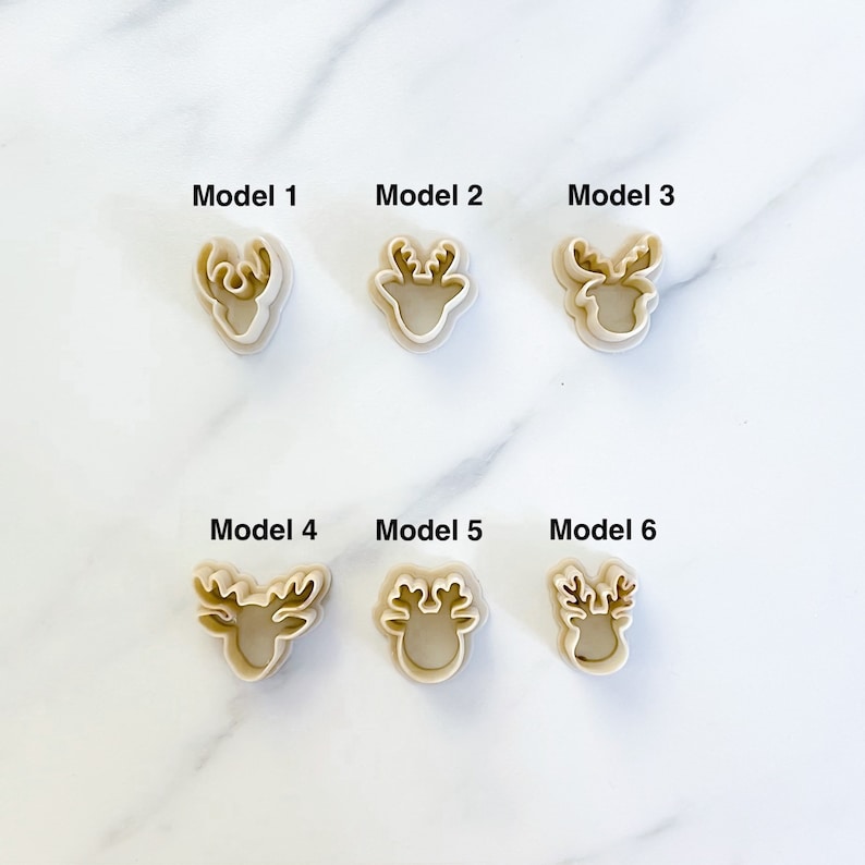 May include: Six beige plastic cookie cutters shaped like deer heads, arranged in two rows of three. Each cutter is labeled with text above it, ranging from Model 1 to Model 6, showing distinct antler designs for each individual deer head shape.