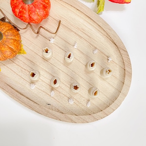 Peut inclure: Un ensemble de neuf petits emporte-pièces en plastique blanc en forme de citrouille sur une surface en bois. Les emporte-pièces sont disposés en rangée, le plus grand à gauche et le plus petit à droite. Il y a aussi plusieurs petites feuilles en plastique blanc éparpillées autour des emporte-pièces.