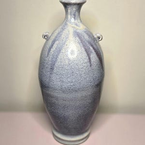May include: A tall, speckled ceramic vase in shades of blue and purple. The vase has a narrow neck, two small handles, and a rounded body. The base is a lighter shade of blue.