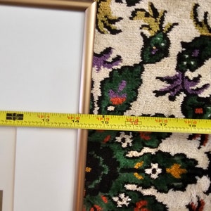 May include: A gold-coloured picture frame with a white mount and a white background. The frame is sitting on a colourful rug with a floral pattern.