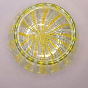 May include: A clear glass bowl with a yellow and white striped design. The stripes radiate from the center in a spiral pattern. The bowl has a rounded shape and a thick rim. The text "УКРАЇНСЬКА" is visible on the side of the bowl.