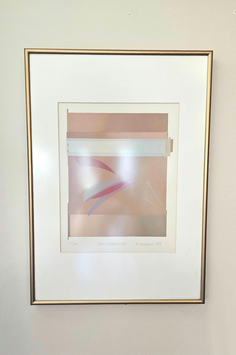 May include: A framed abstract art print with a pale pink, white, and grey colour scheme. The print features geometric shapes and lines, with a subtle texture. The artist's signature and date are visible in the lower right corner.