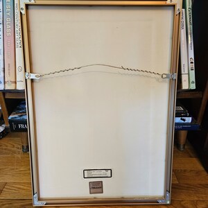 May include: A gold-coloured picture frame with a white mount and a white background. The frame has a wire hanger on the back and a sticker that says "Professionally Framed by Michaels".