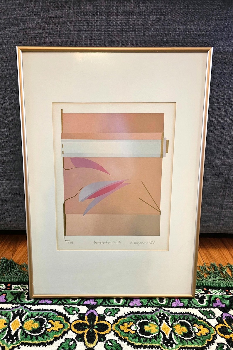 May include: A framed abstract art print with a geometric design in shades of pink, brown, and white. The print is titled "French Memorial" and signed "E. Dagnan 1983".