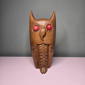 May include: A wooden owl figurine with red eyes. The owl is carved with detailed feathers and a beak.