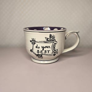 May include: A white ceramic mug with a black handle and the text "But First, Coffee" in a bold, black font. The mug is set against a blurred background, suggesting a cozy setting. The mug appears to be approximately 4 inches tall.