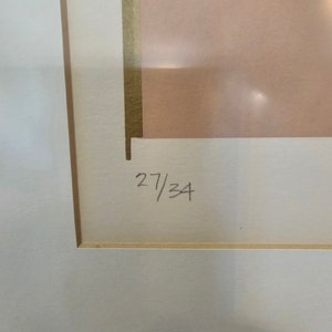 May include: A close-up of a white mount with a gold border. The number "27/34" is written in black ink on the mount.