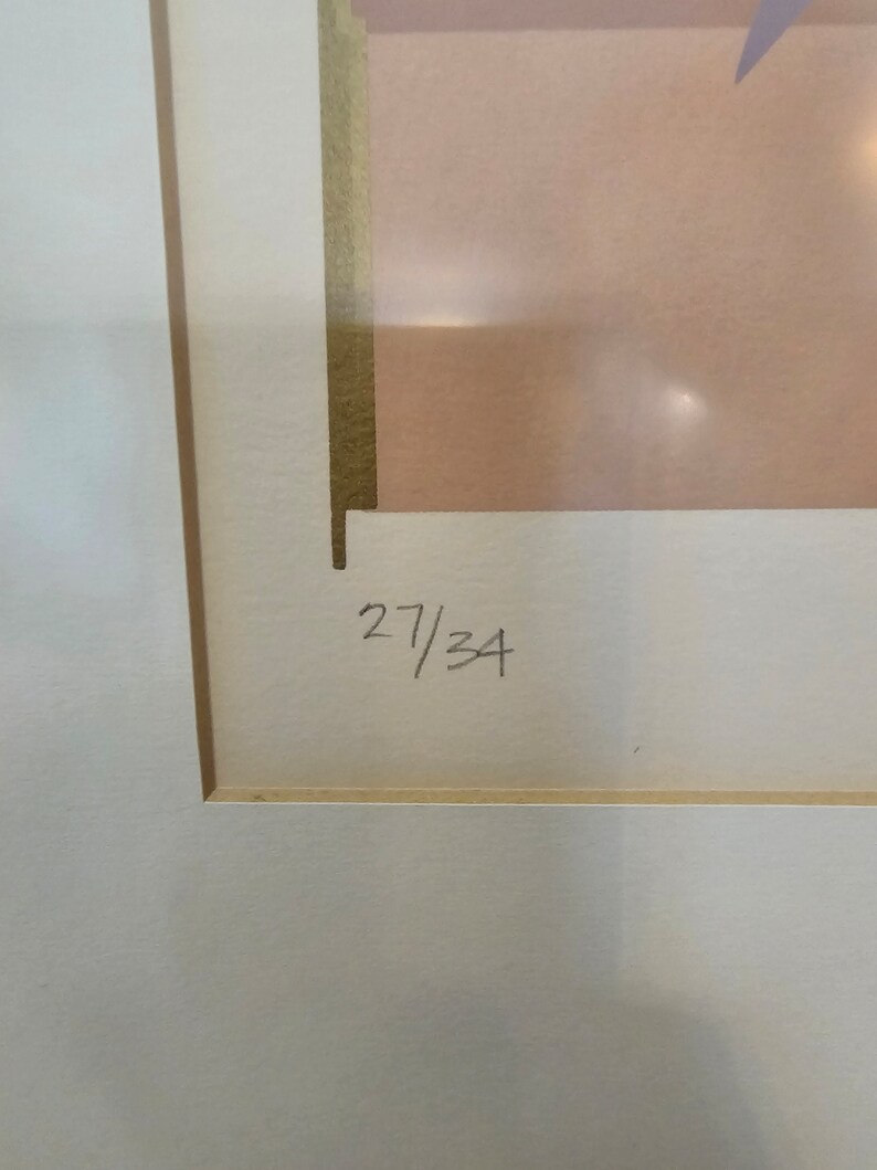 May include: A close-up of a white mount with a gold border. The number "27/34" is written in black ink on the mount.