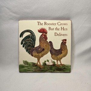 May include: Square ceramic tile featuring a rooster and hen illustration with the text "The Rooster Crows But the Hen Delivers." The rooster has a red comb and a green and black tail. The hen is brown and gold.
