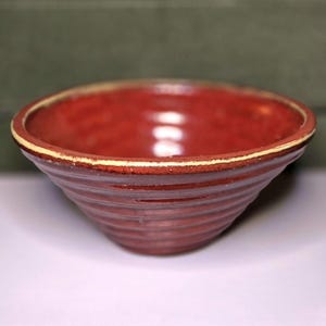 May include: A red ceramic bowl with a white rim and a ribbed design. The bowl is empty and has a glossy finish.