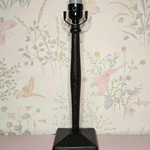 May include: A black table lamp with a textured, woven-like design on the stem. The lamp has a square base and a black lamp holder. The lamp is approximately 15 inches tall.