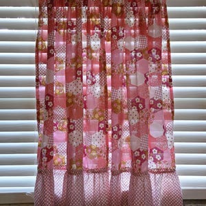 May include: A window curtain featuring a patchwork design of pink, white, and yellow hexagonal patterns with floral, polka dot, and grid motifs. The curtain has a gathered top rod pocket and a wide, ruffled bottom hem with a white and red grid print.