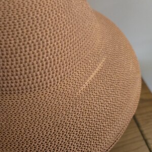 May include: Close-up of a tan hat featuring a textured, woven design. The hat's surface has a repeating geometric pattern, giving it a tactile feel. The hat's shape is rounded, indicating a casual style.