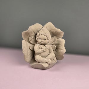 May include: A beige-colored fairy figurine, sculpted in a seated position within a large flower. The fairy has detailed wings and a serene expression. The flower's petals are intricately designed, creating a whimsical and decorative piece.