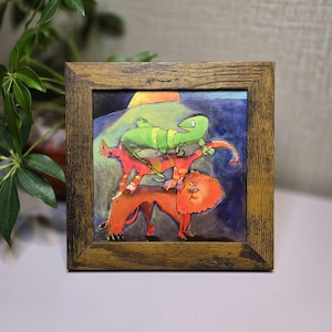 May include: Square framed artwork featuring a whimsical illustration of a lion, a fox, and a lizard stacked on top of each other. The artwork has a dark blue background with a yellow sun. The frame is made of wood.