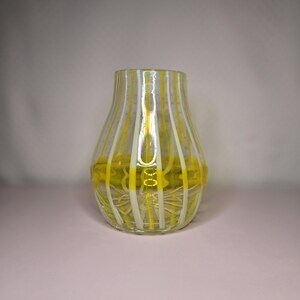 May include: A clear glass vase with vertical stripes of yellow and white. The vase has a rounded body and a slightly flared opening. The bottom of the vase has a yellow design. The vase is likely used for decorative purposes.