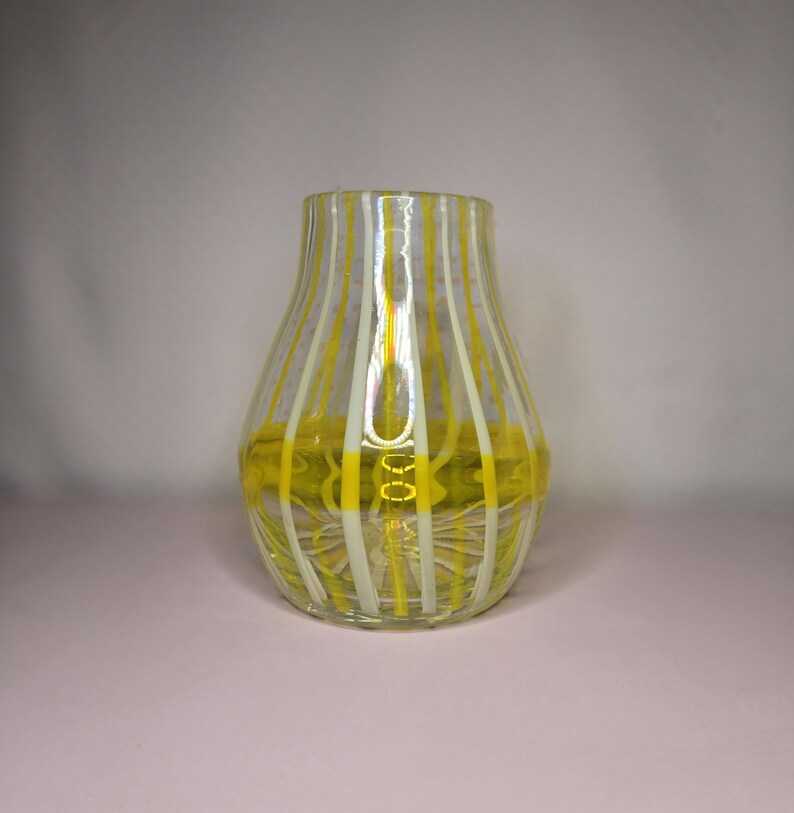 May include: A clear glass vase with vertical stripes of yellow and white. The vase has a rounded body and a slightly flared opening. The bottom of the vase has a yellow design. The vase is likely used for decorative purposes.